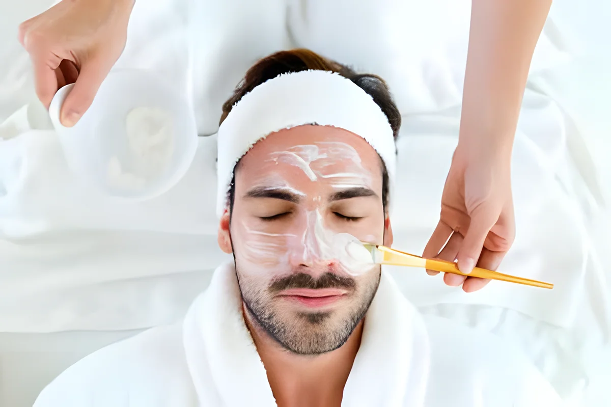 Mann erhält Gesichtsbehandlung mit Creme und Pinsel.
